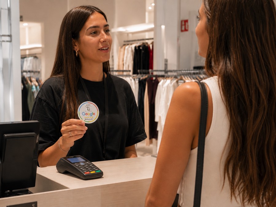 Dependienta mostrando la placa NFC a una clienta en el mostrador de una tienda de ropa